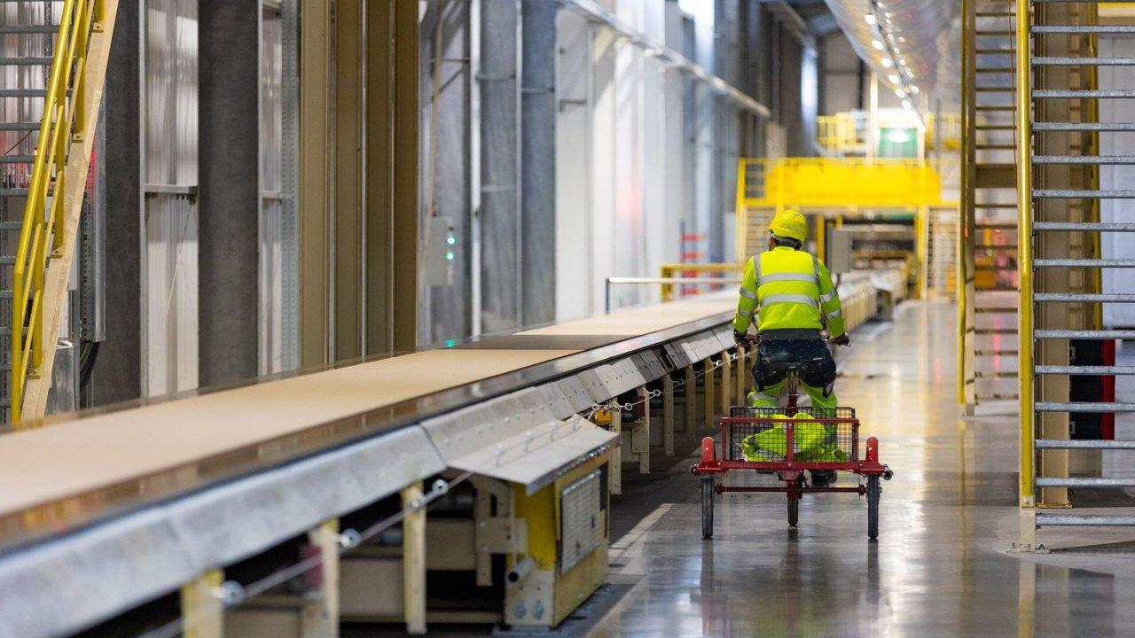 Factory worker in high-visibility clothing rides a trolley beside a production line.
