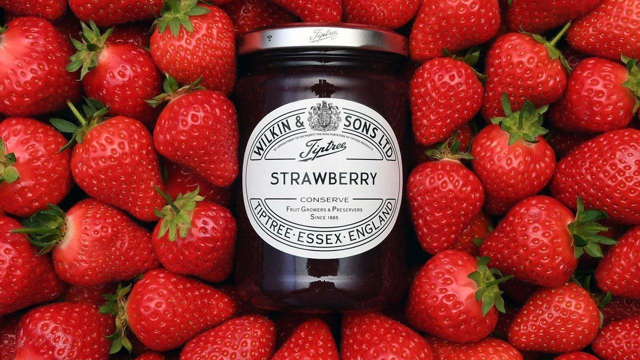 A jar of Tiptree strawberry conserve surrounded by fresh strawberries