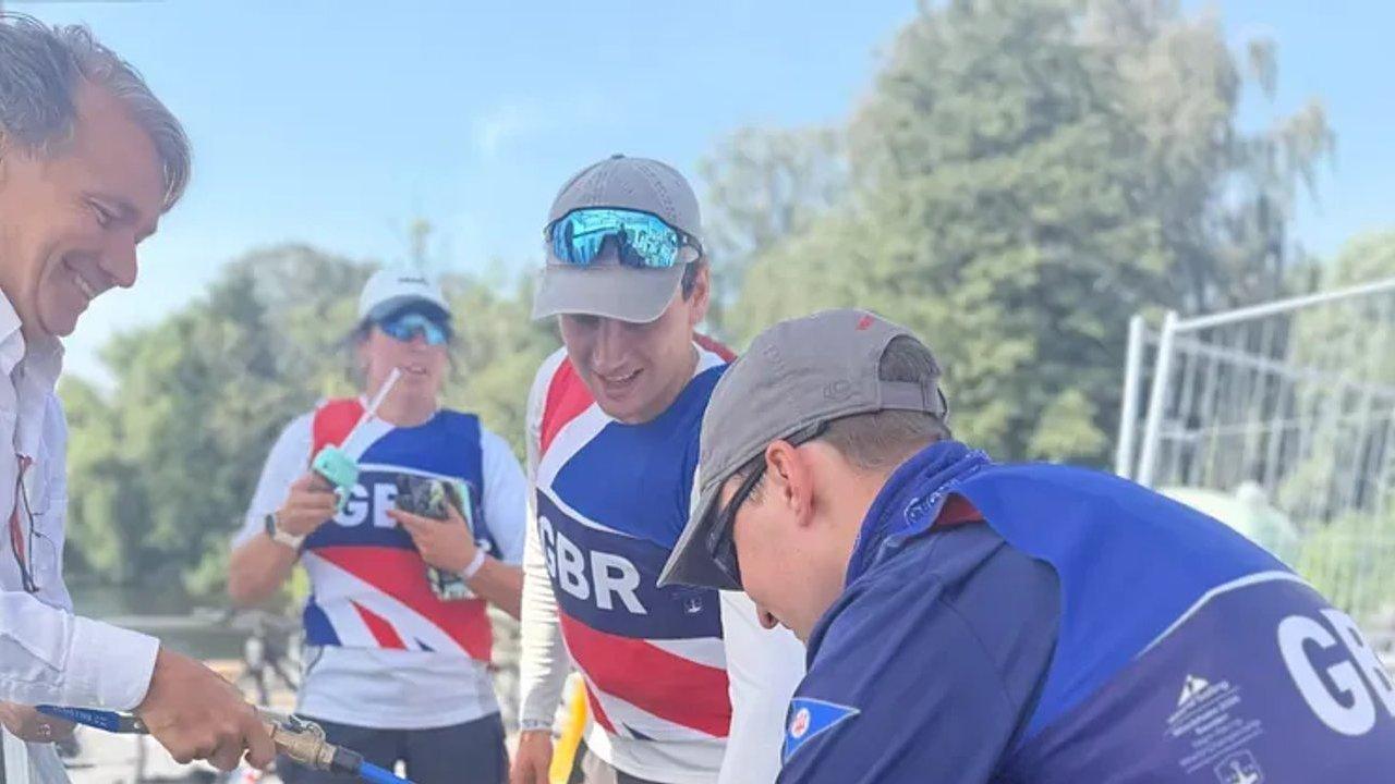 Four men in GBR uniforms gather around equipment outdoors, with trees behind them.