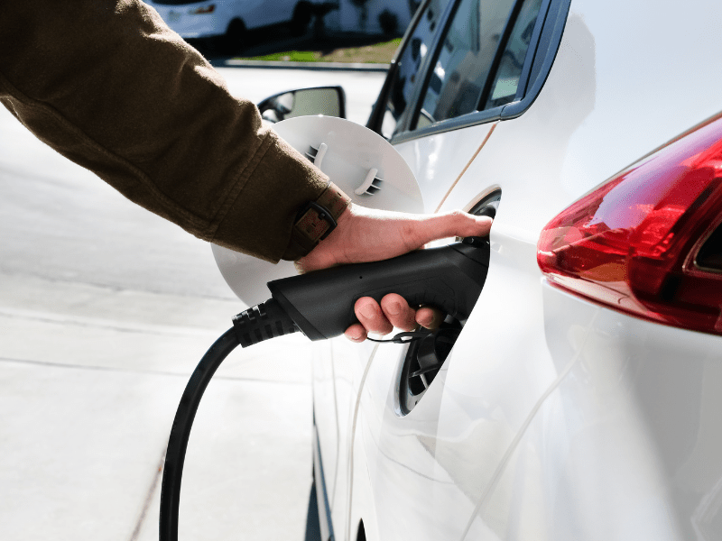 A person plugging a charging connector into the port of a white electric car on a driveway