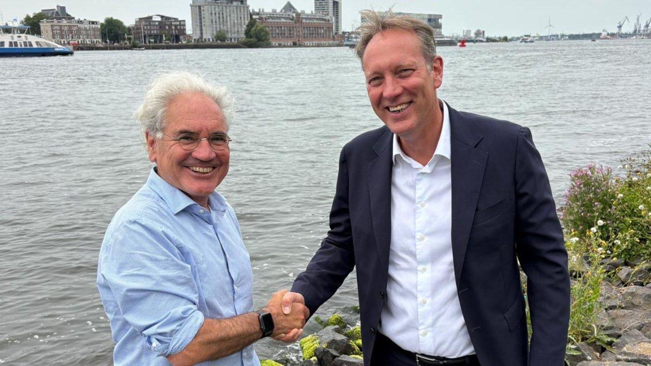 Govert Meijer and Frank Koopman shake hands beside a river.