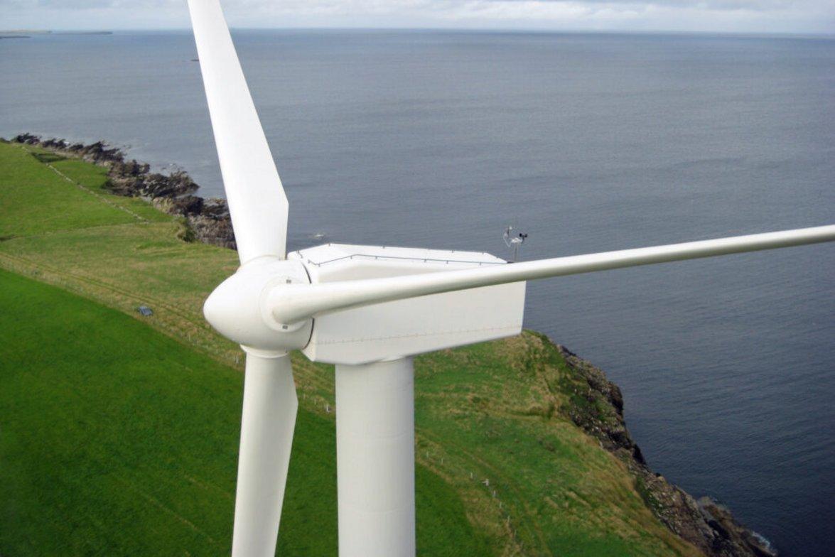 White wind turbine on a green coastal cliff under a cloudy sky, symbolising renewable energy crowdfunding projects