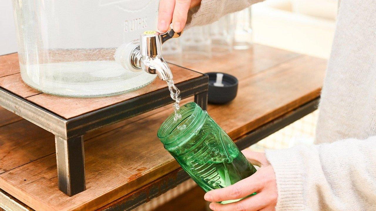 Hands refilling a reusable green water bottle from a glass dispenser, symbolising sustainable practices