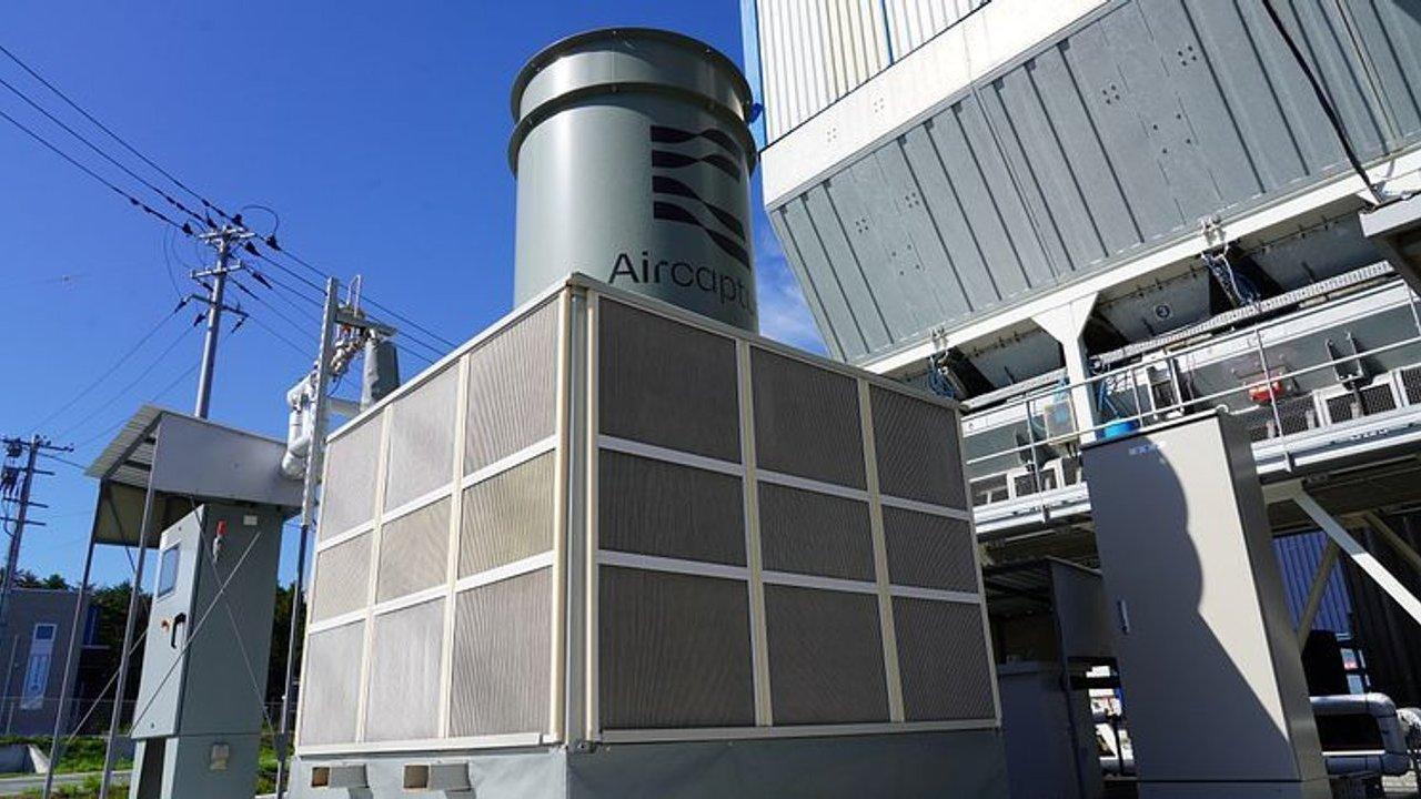 Industrial air cooling unit beside electrical equipment and a large metal building under a blue sky