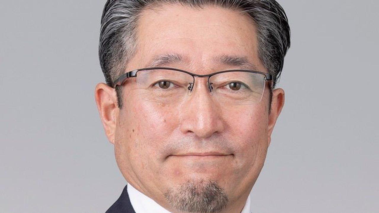 Headshot of a man wearing glasses, a suit and tie against a gray background