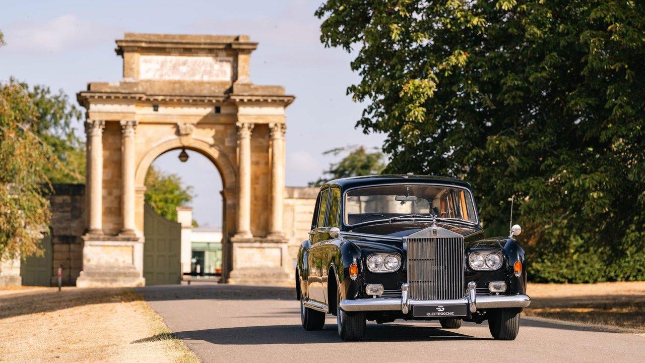 A black Rolls-Royce parked on a driveway before a stone archway and trees
