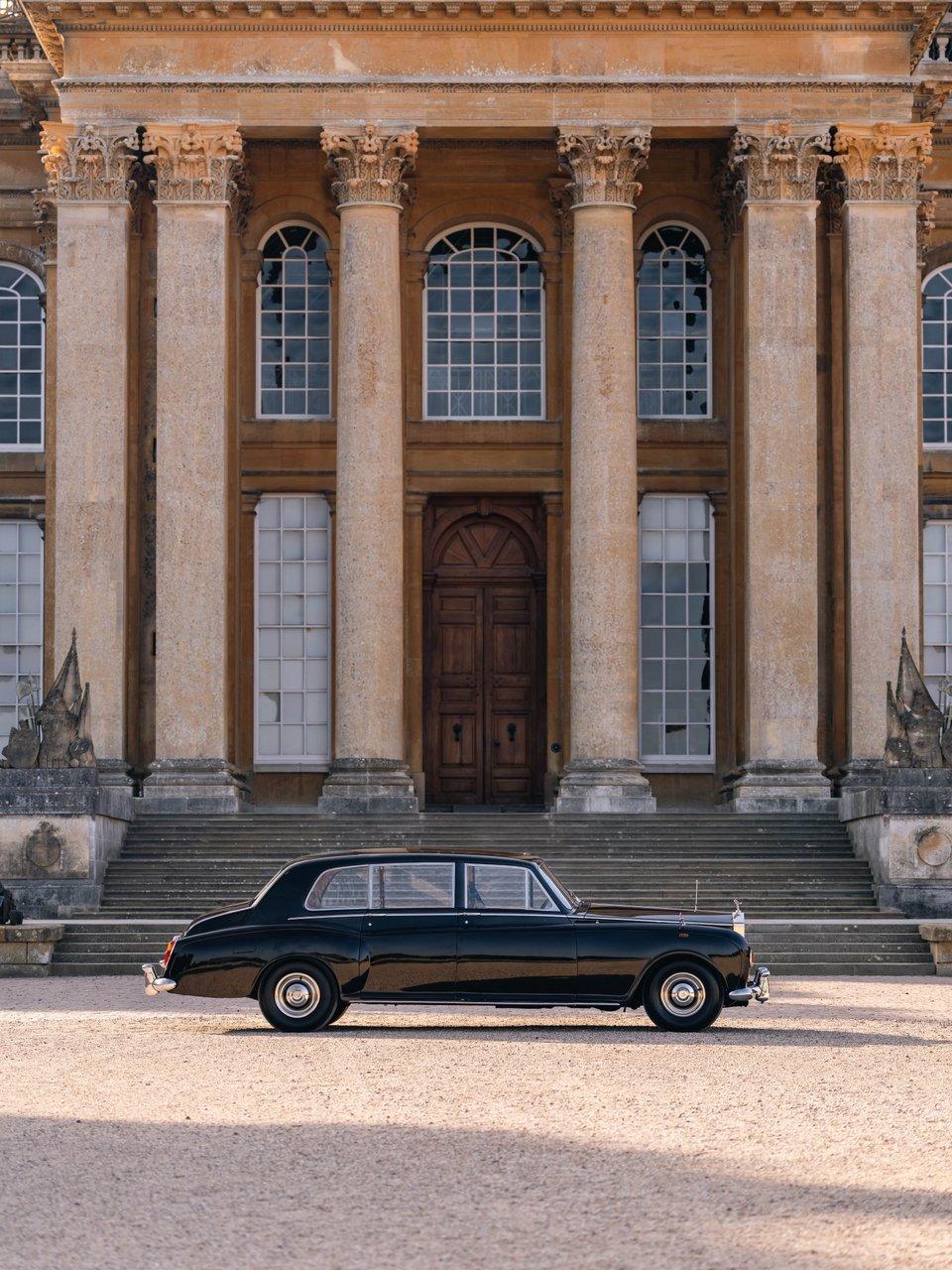 A black vintage limousine parked before a grand stone building with Corinthian columns and wide steps.