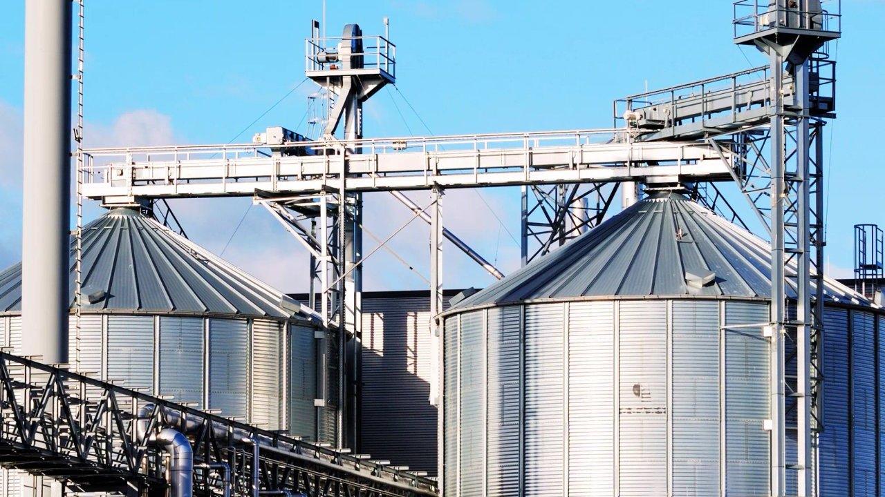 Metal grain silos linked by elevated conveyor belts under a blue sky