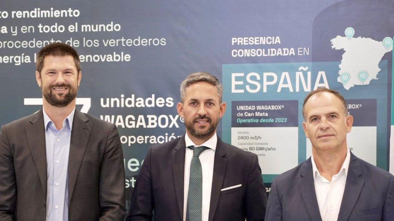 Three men in business suits stand before a Spanish WAGABOX presentation display.