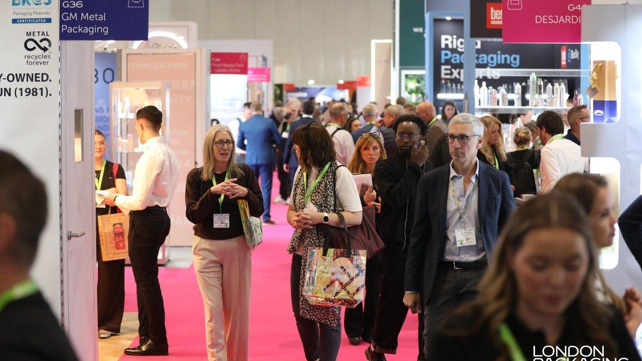 Crowd of attendees walking through a packaging trade show aisle with exhibitor booths and signs.