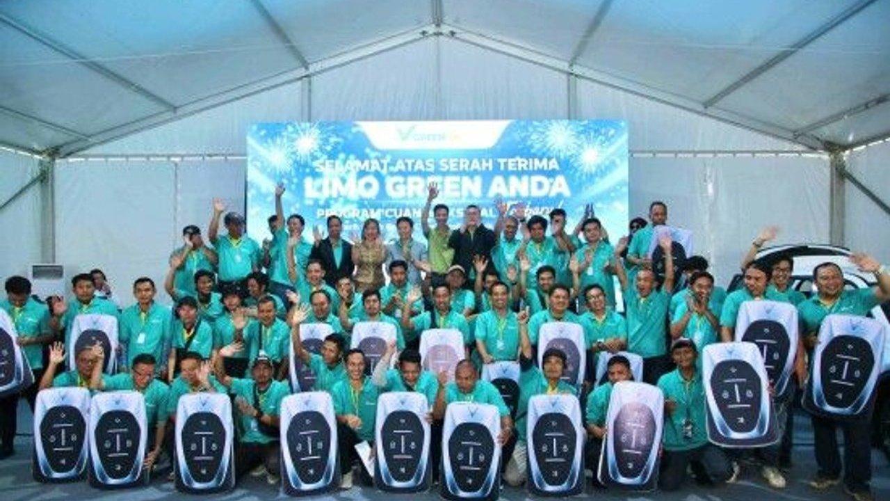 Group of people in turquoise shirts holding large car key signs under a tent.