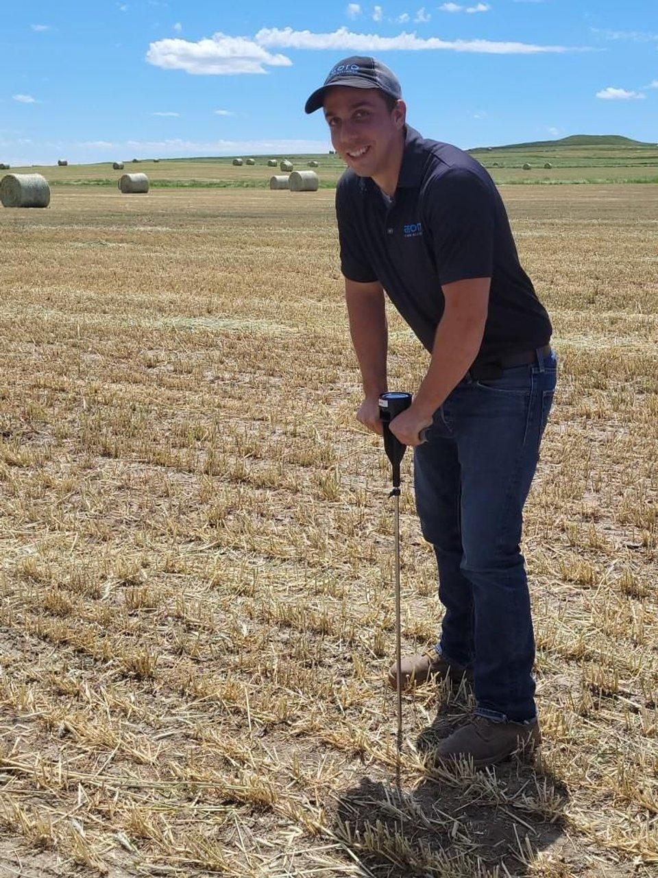 Steve Hasselman uses a penetrometer in a harvested field with hay bales.
