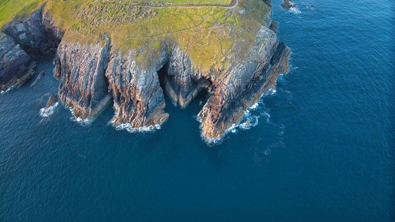 Rocky sea cliffs topped with grassy land, surrounded by blue water.