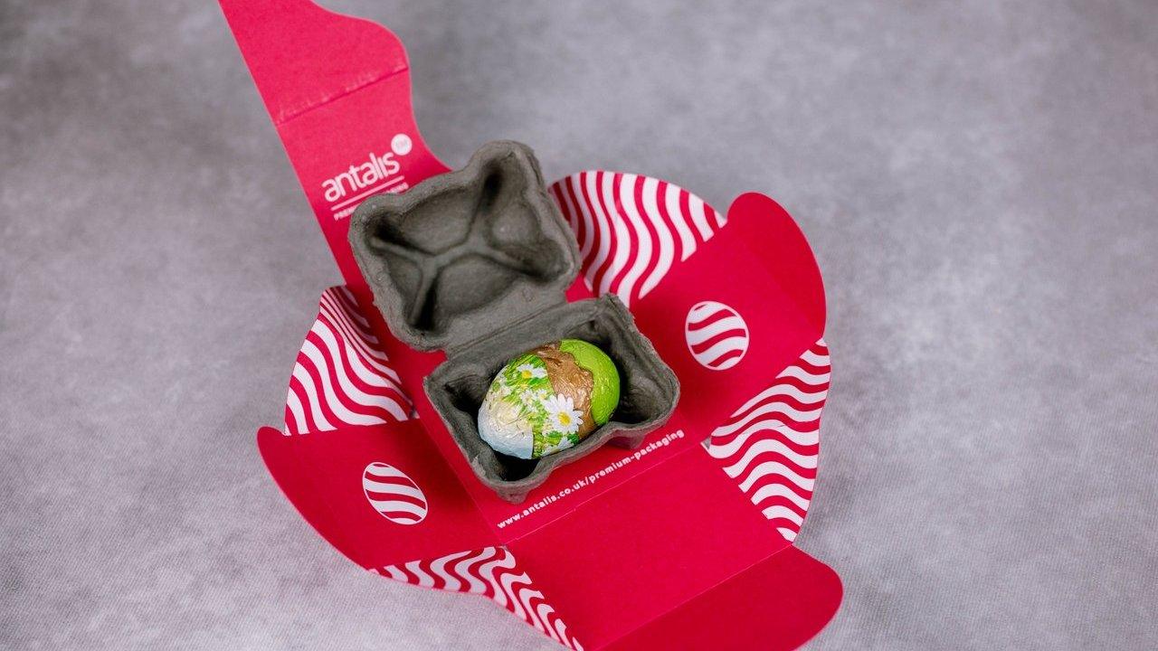A decorated chocolate egg in a small grey egg box inside red presentation packaging