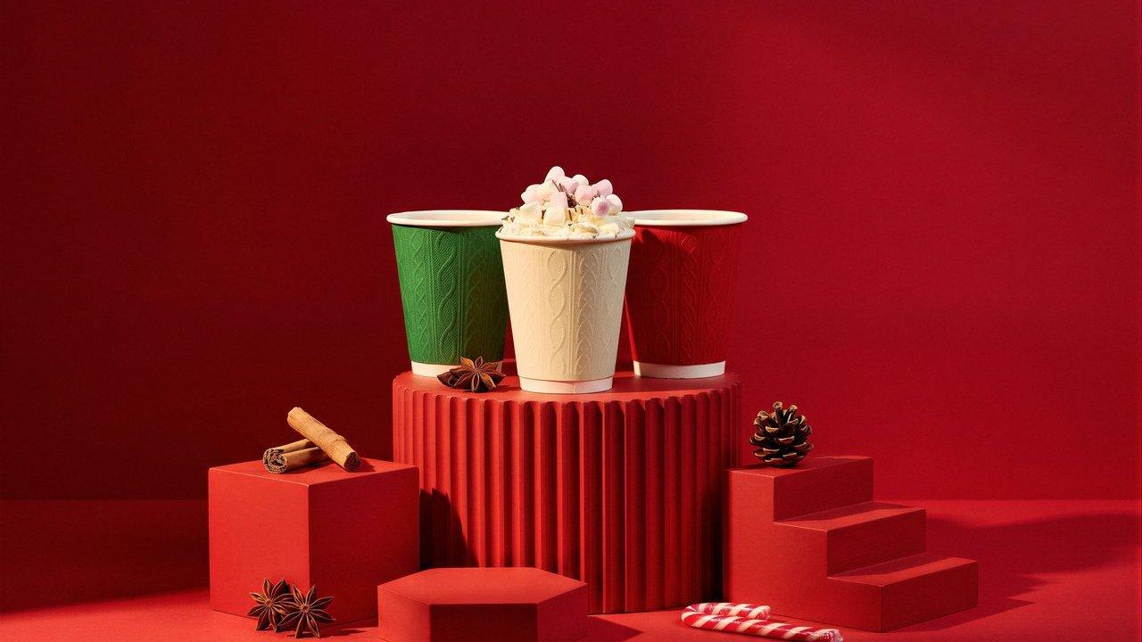 Three festive green, cream and red paper cups on red plinths with cinnamon, star anise and a pinecone