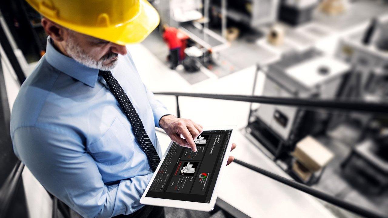 Man in a hard hat checks machinery monitoring data on a tablet in an industrial facility.