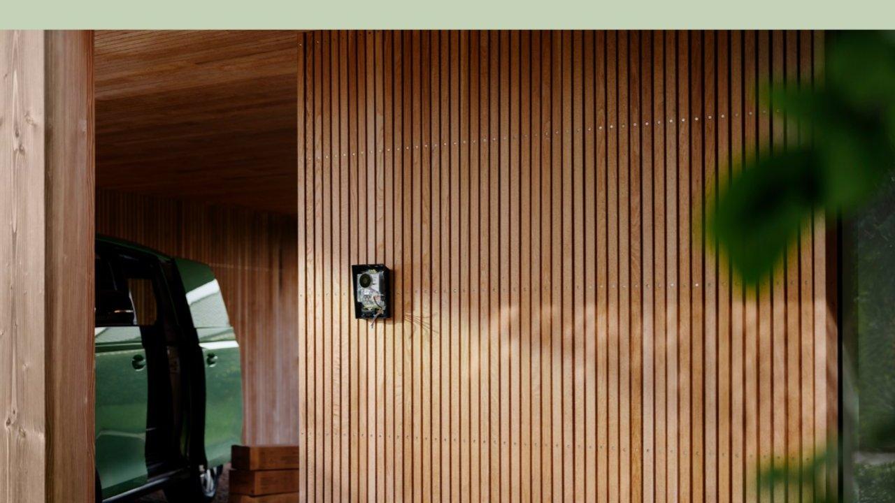 A car parked in a wood-paneled garage beside a wall-mounted security camera.