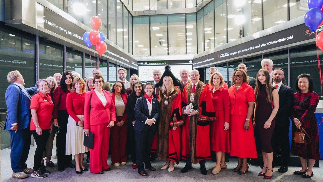Group of people in red and black outfits at the London Stock Exchange with red and blue balloons.