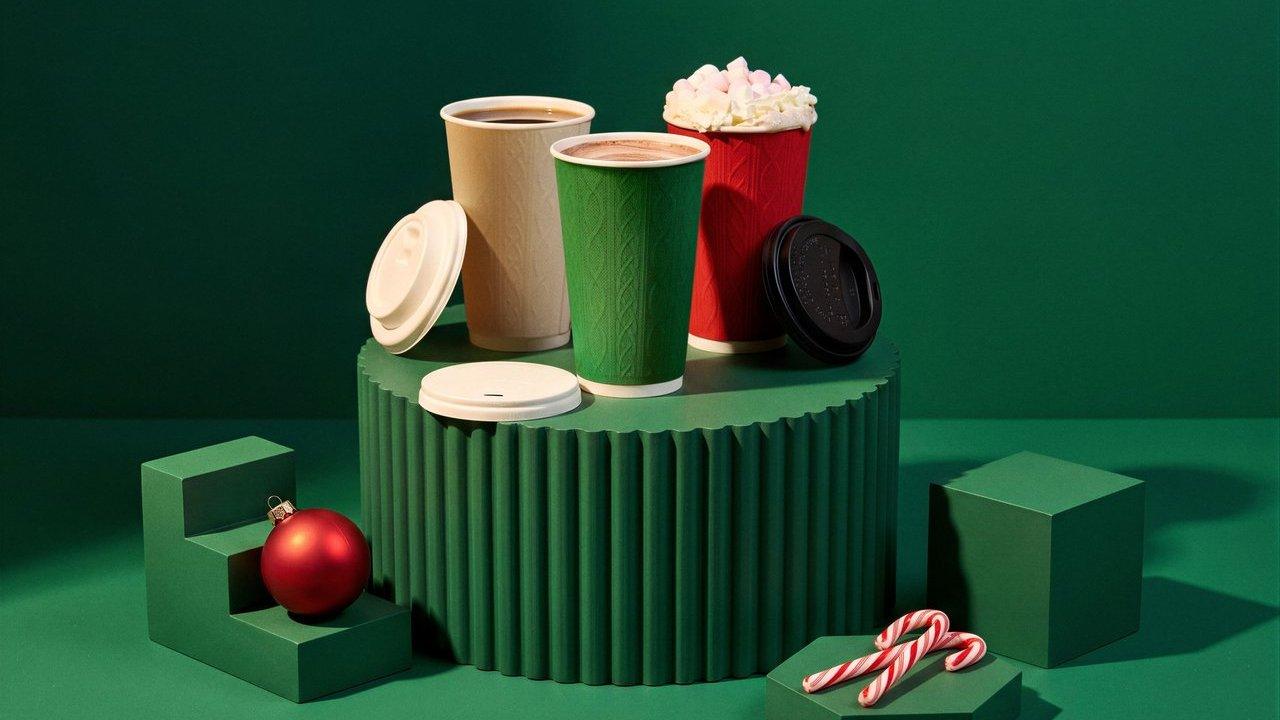 Three festive takeaway drink cups with lids, candy canes and a red bauble on green pedestals
