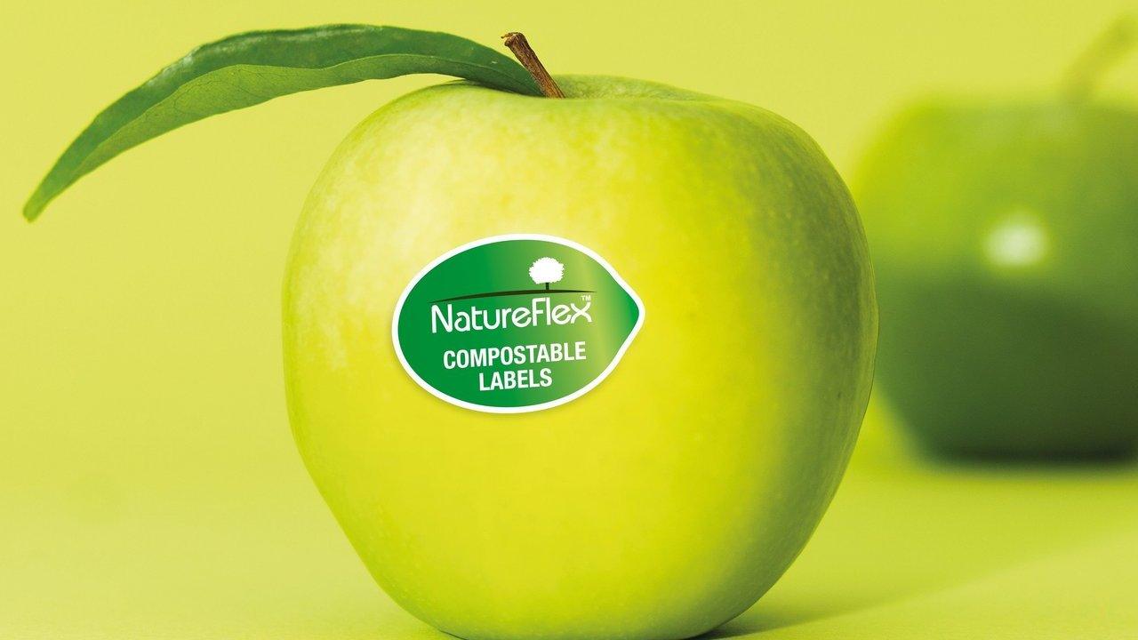 A green apple with a NatureFlex compostable labels sticker and leaf.