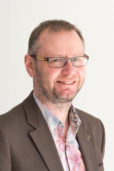 Prof Kevin Daniels wearing glasses, a brown blazer and a patterned shirt.