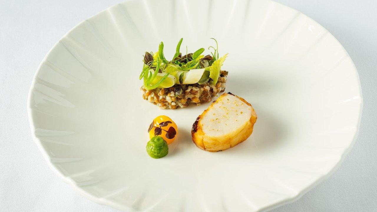 Seared scallop with vegetable tartare, microgreens and green and orange purées on a white plate