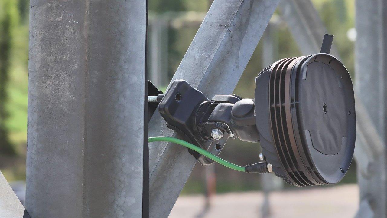 Black circular sensor mounted on a metal support with a green cable attached.