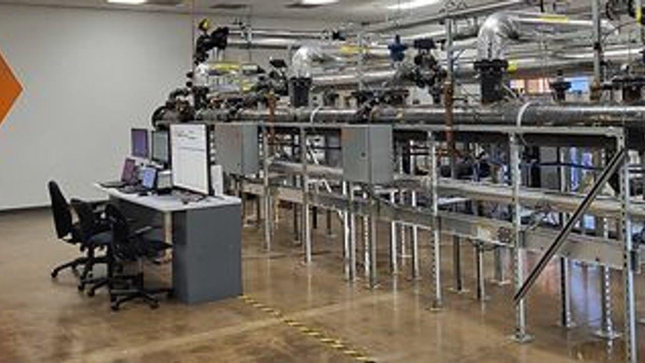 Industrial demo center with pipework, control monitors and office chairs.