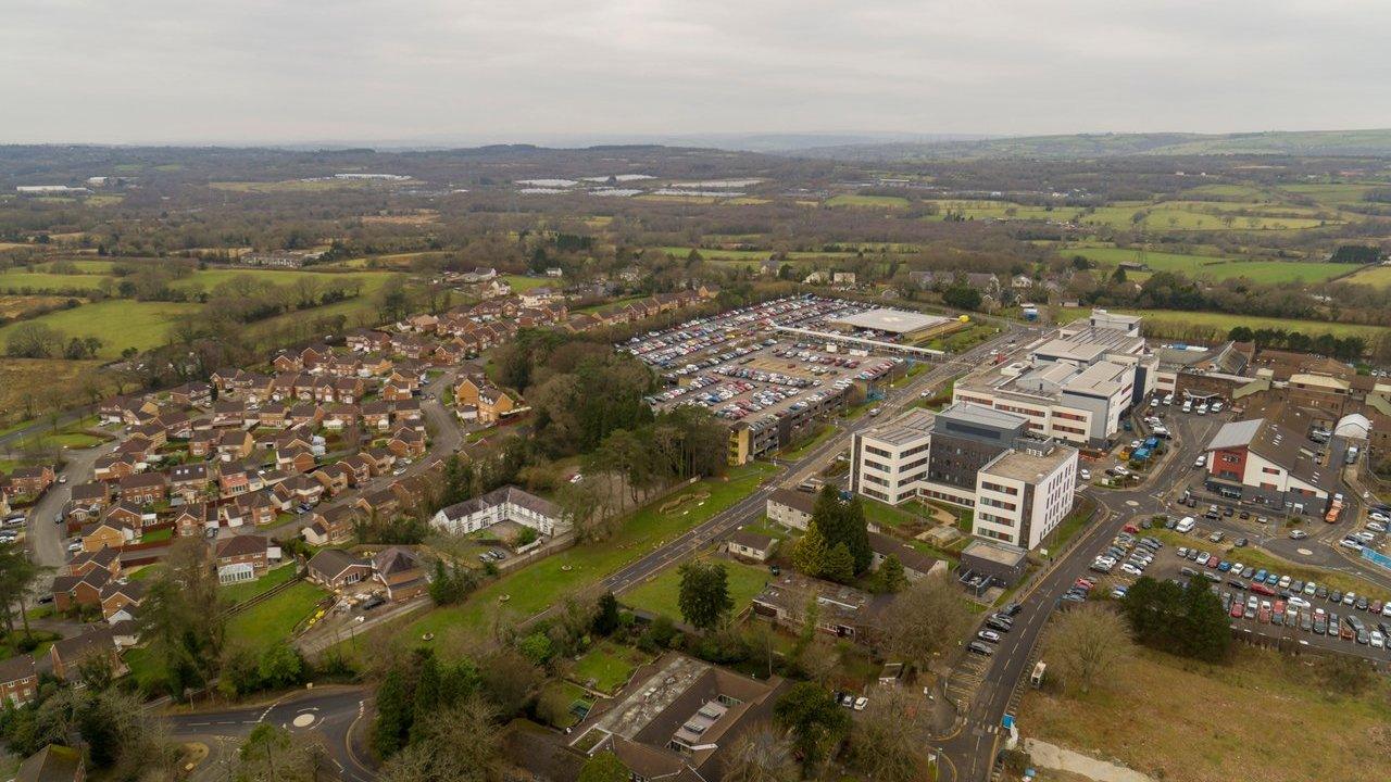 Aerial view of Morriston Hospital buildings, car parks and surrounding homes and countryside