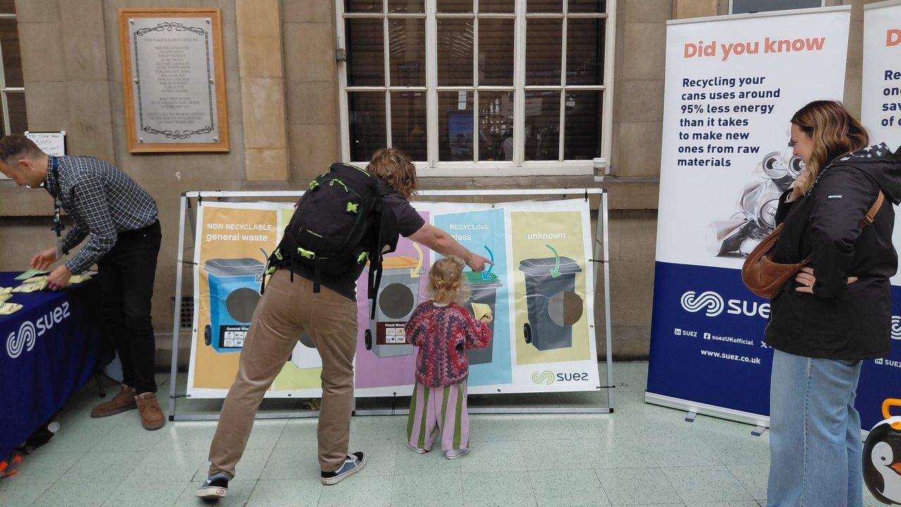 People at a recycling roadshow using a bin-sorting display beside SUEZ information banners
