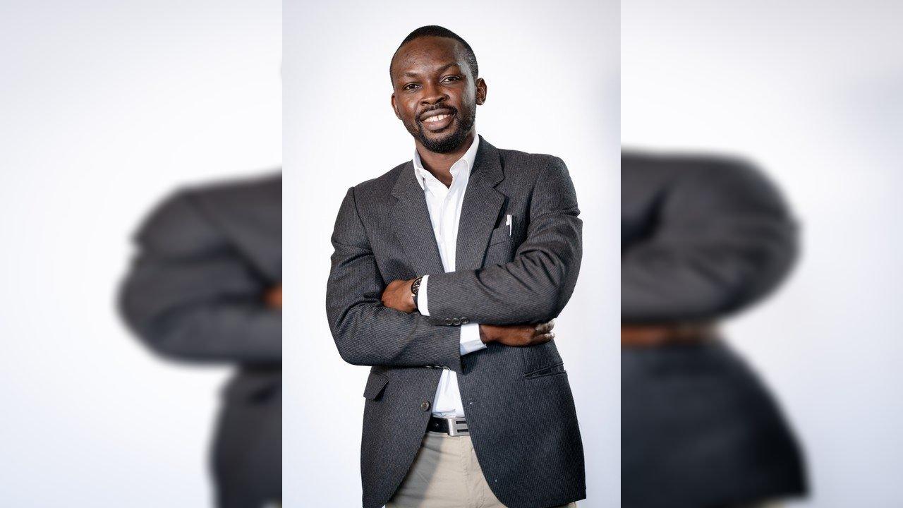 Patrick Umeadi smiling with arms crossed, wearing a dark suit jacket and white shirt.