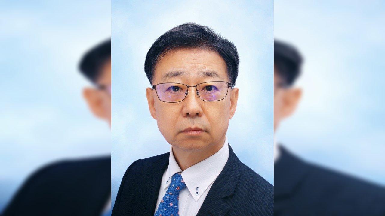Professor Norio Shibata in glasses, a dark suit and blue tie against a pale blue background.