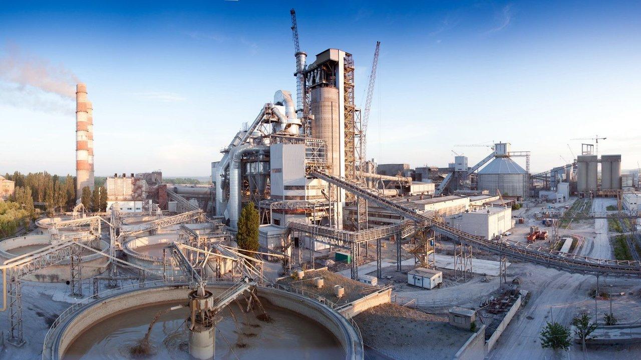 Cement plant with smokestack, conveyors, silos and circular settling tanks under a blue sky
