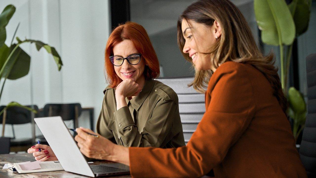 Two women reviewing documents beside a laptop at a table.