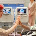 An airline attendant high-fives a smiling child in a wheelchair beside aircraft seats.