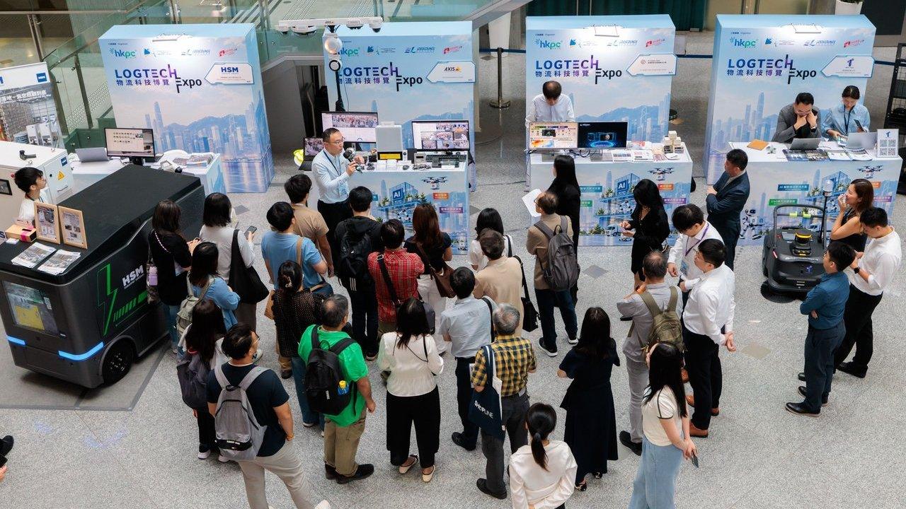 Crowd watching a robotics demonstration at LOGTECH Expo booths, with autonomous delivery robots on display.