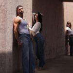 Three people in white tops and jeans stand in a sunlit concrete corridor.