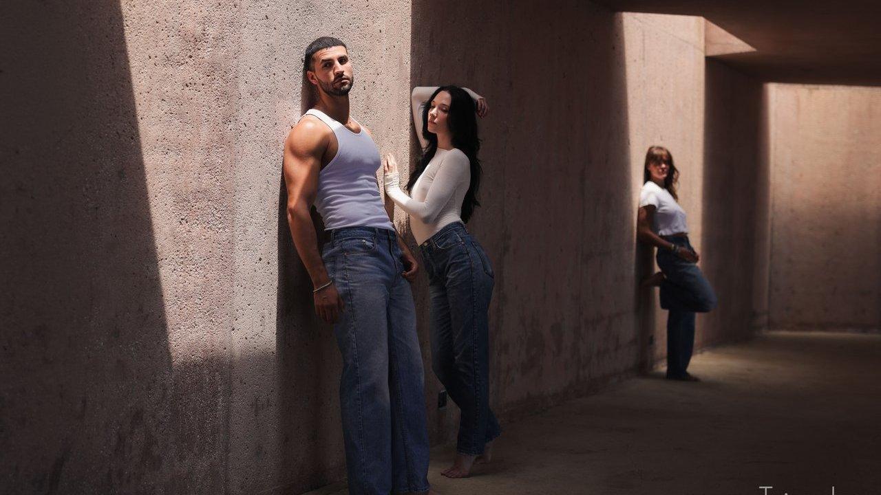 Three people in white tops and jeans stand in a sunlit concrete corridor.