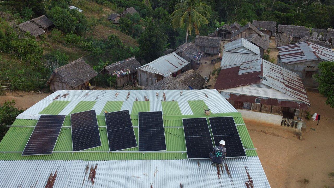Solar panels on a corrugated metal roof above a rural village with thatched and metal-roofed houses