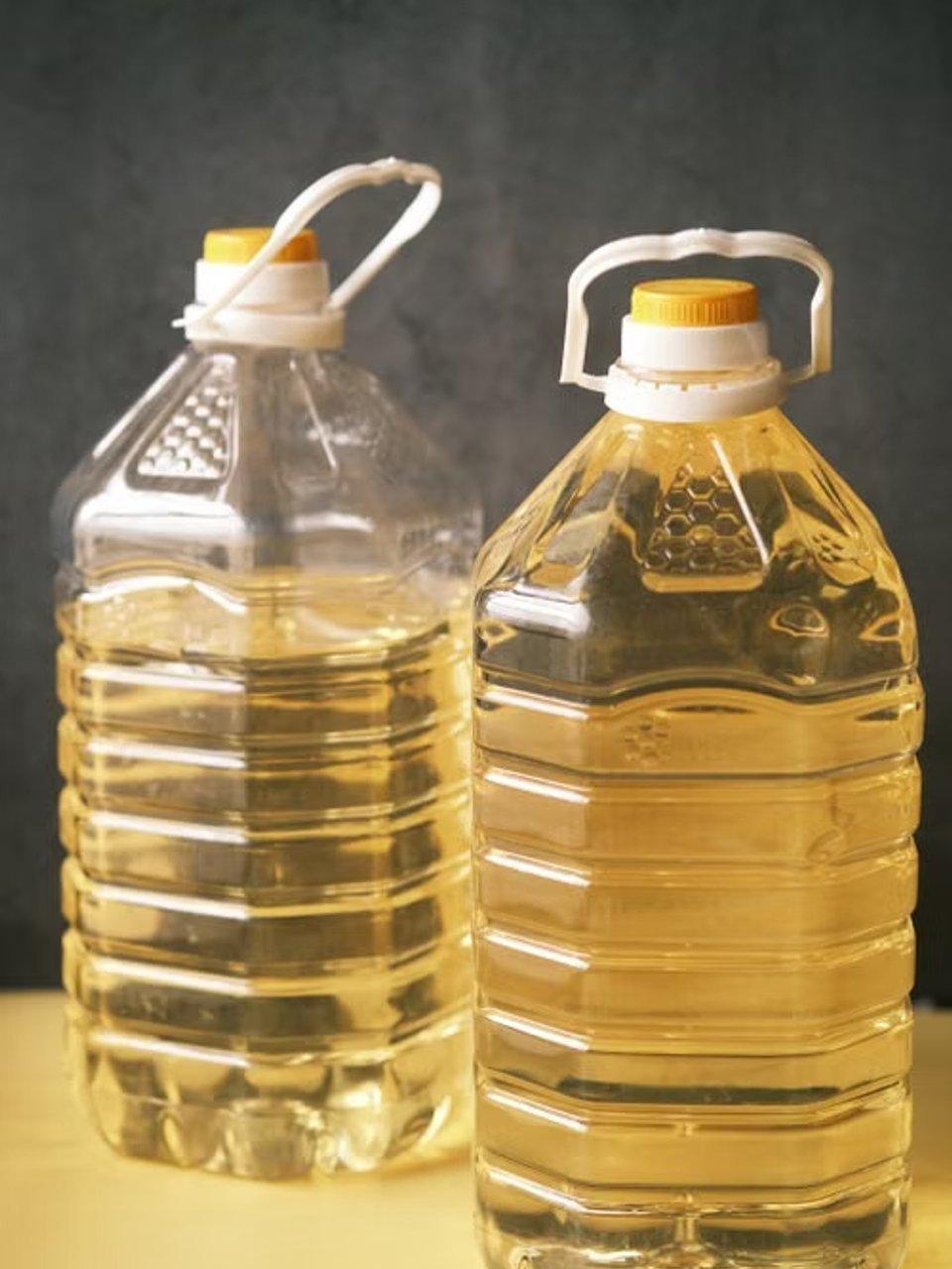 Two large plastic bottles filled with cooking oil, each with a yellow cap and carrying handle.