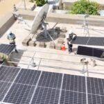 Workers in safety gear install solar panels on a rooftop.
