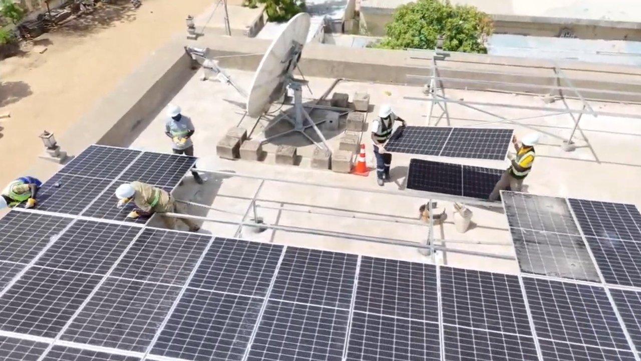Workers in safety gear install solar panels on a rooftop.