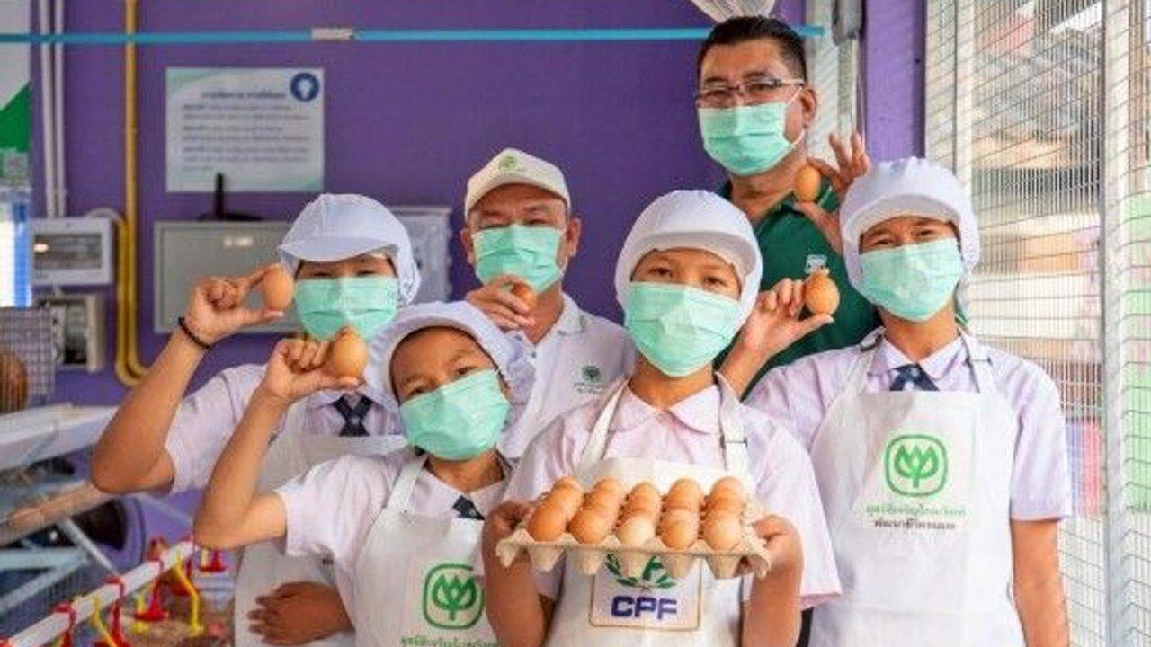 Six masked workers in uniforms hold eggs and a tray of eggs in a poultry facility.