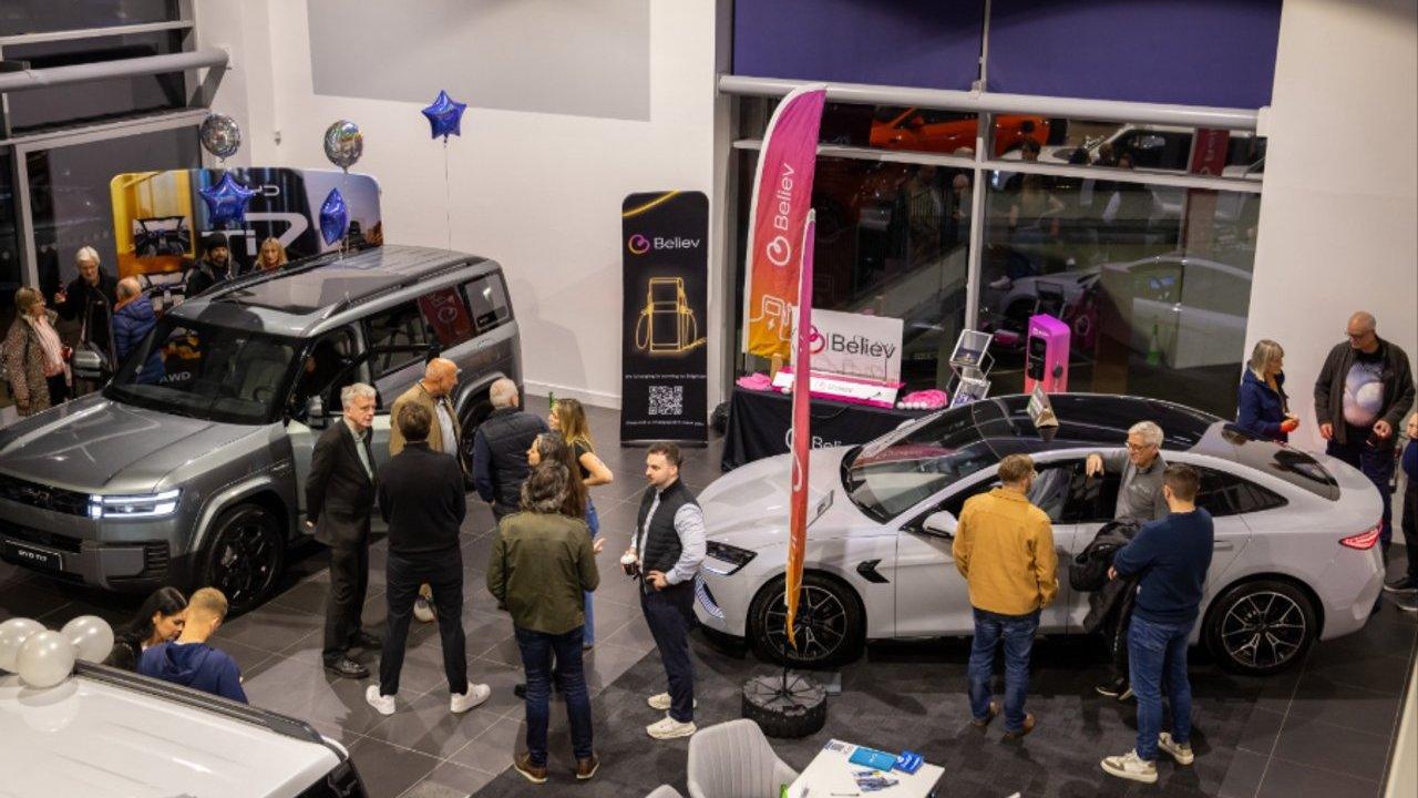 People gather around gray and white electric SUVs at a car dealership event.