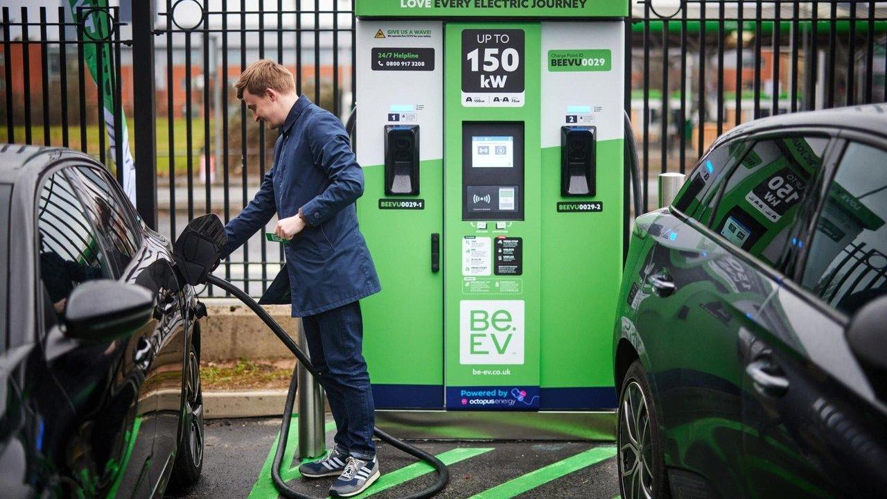 Man charging a black electric car at a green Be.EV charging station between two cars