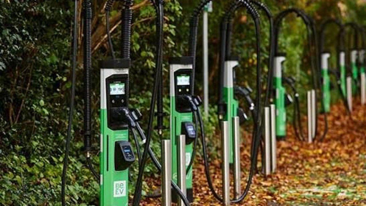 A row of green electric vehicle charging stations beside a leafy path.