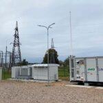 Battery energy storage units beside an electrical substation and transmission towers.