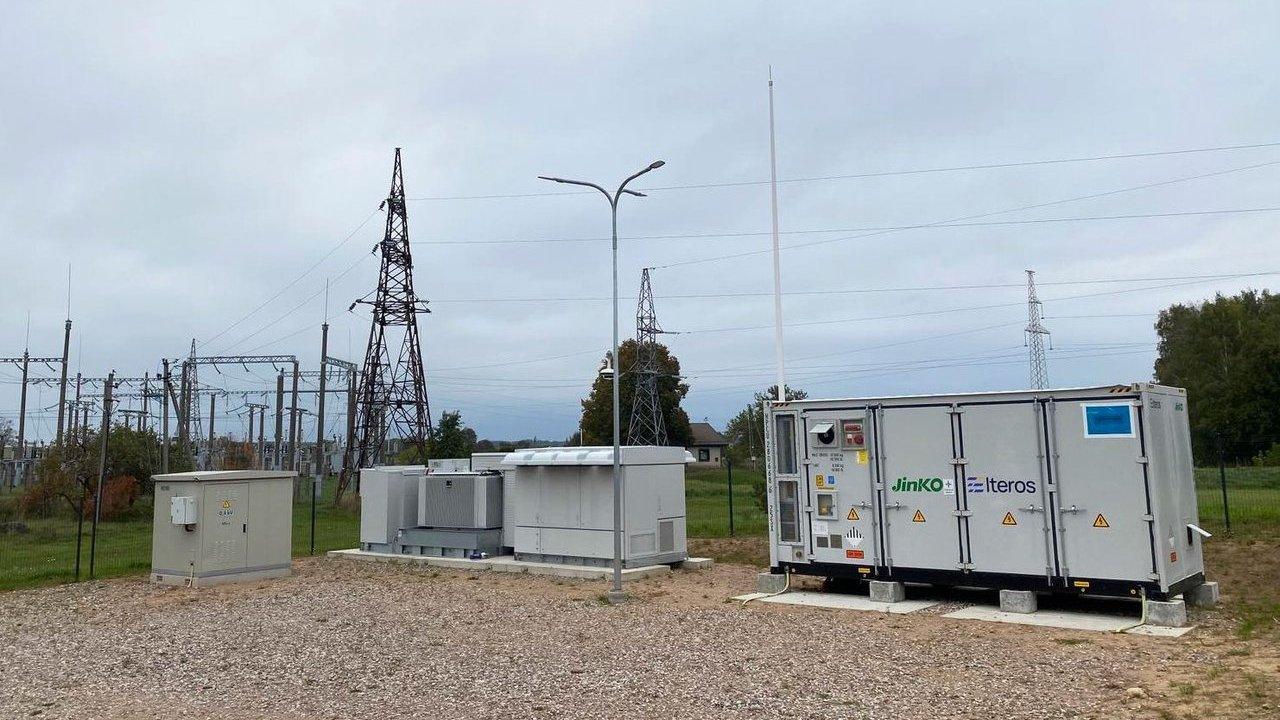 Battery energy storage units beside an electrical substation and transmission towers.