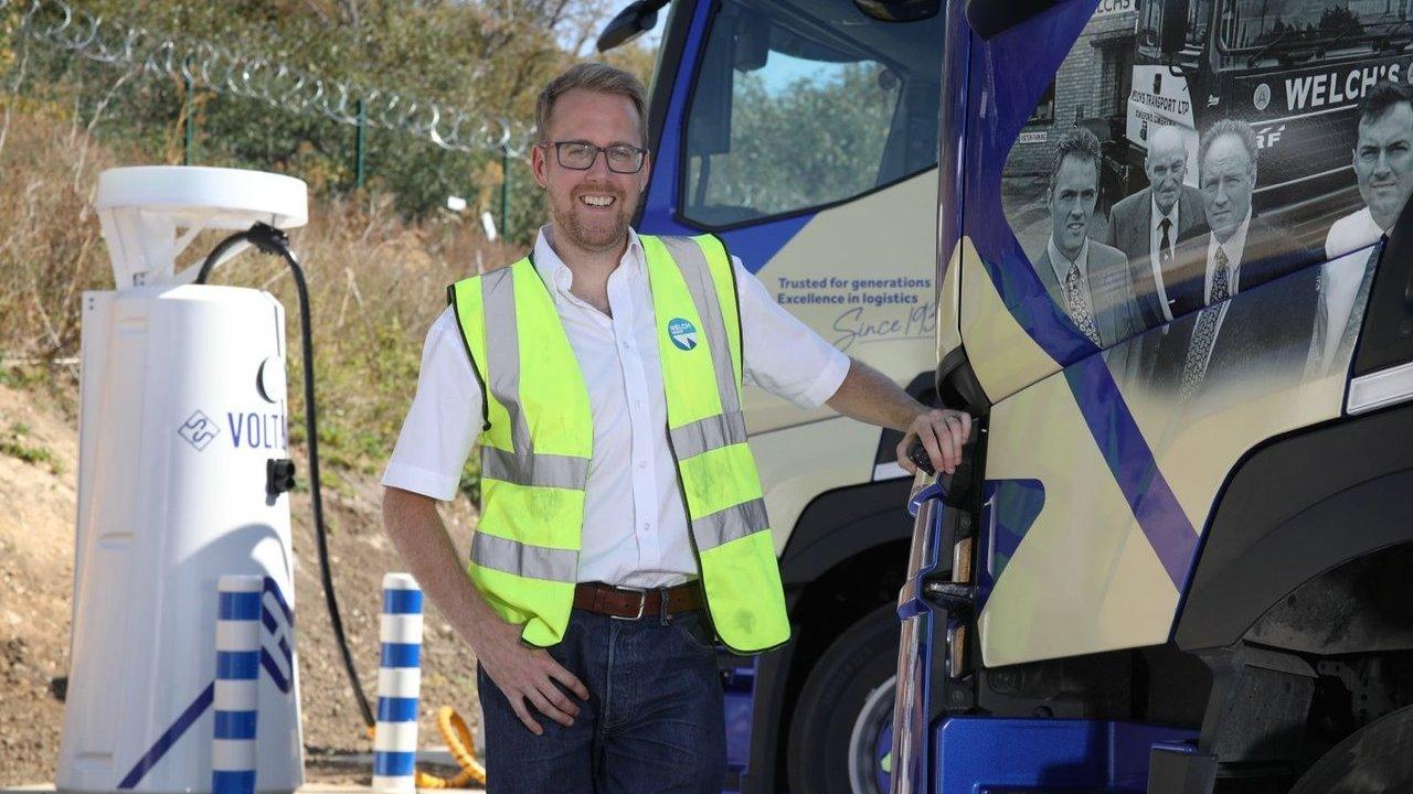Chris Welch in a high-visibility vest charging an electric lorry beside a charging station.