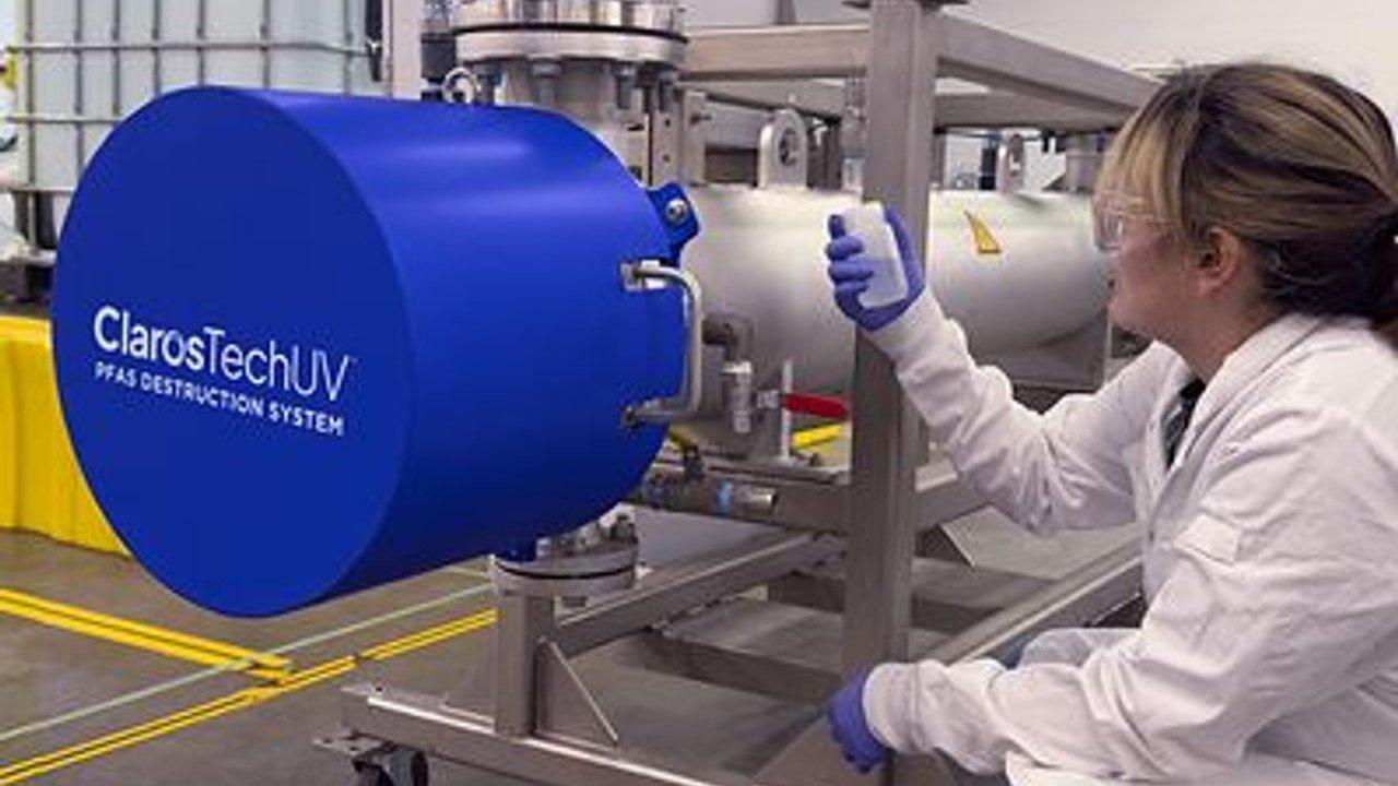 Lab worker holding a sample bottle beside a ClaroTech UV PFAS destruction system
